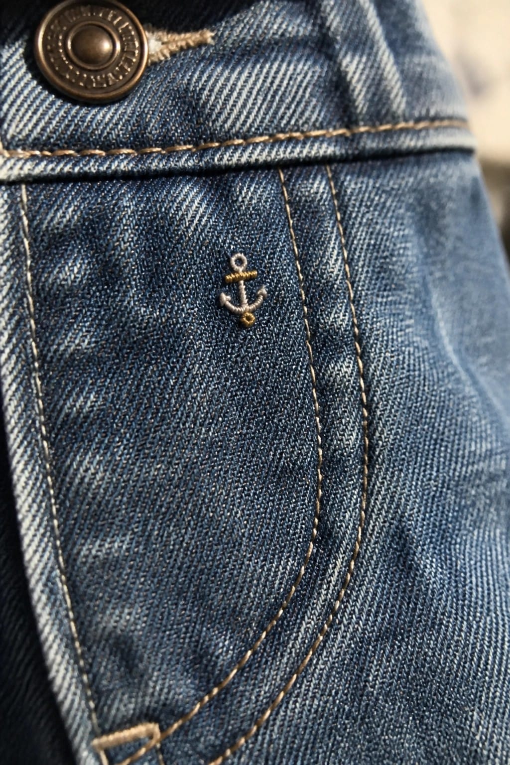 Small embroidered cactus in a brown pot on light blue denim near a seam.
