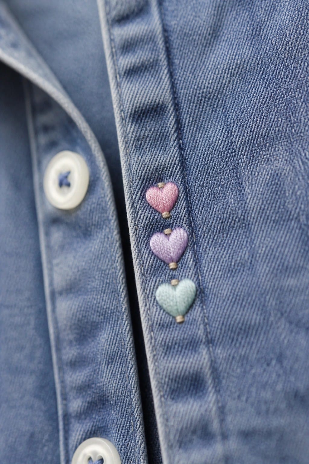 Blue denim jeans with green four-leaf clover embroidery, brown stitching, and metal button.