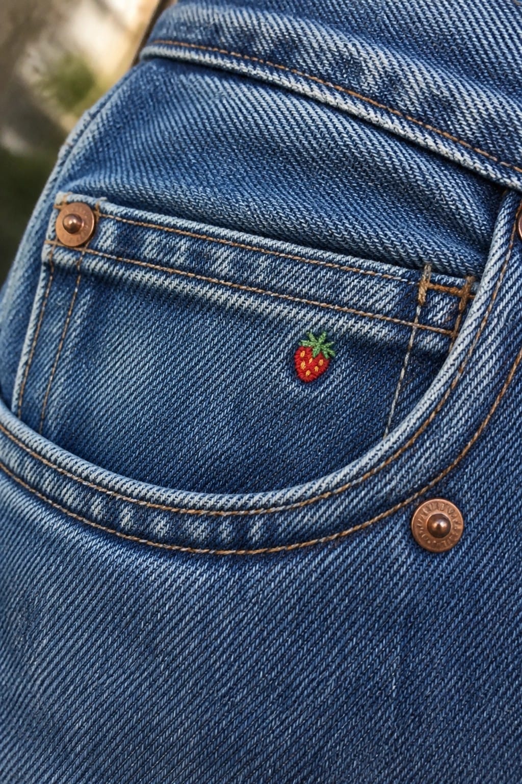 Blue denim jeans with red, pink, and yellow mushroom embroidery near knee rip