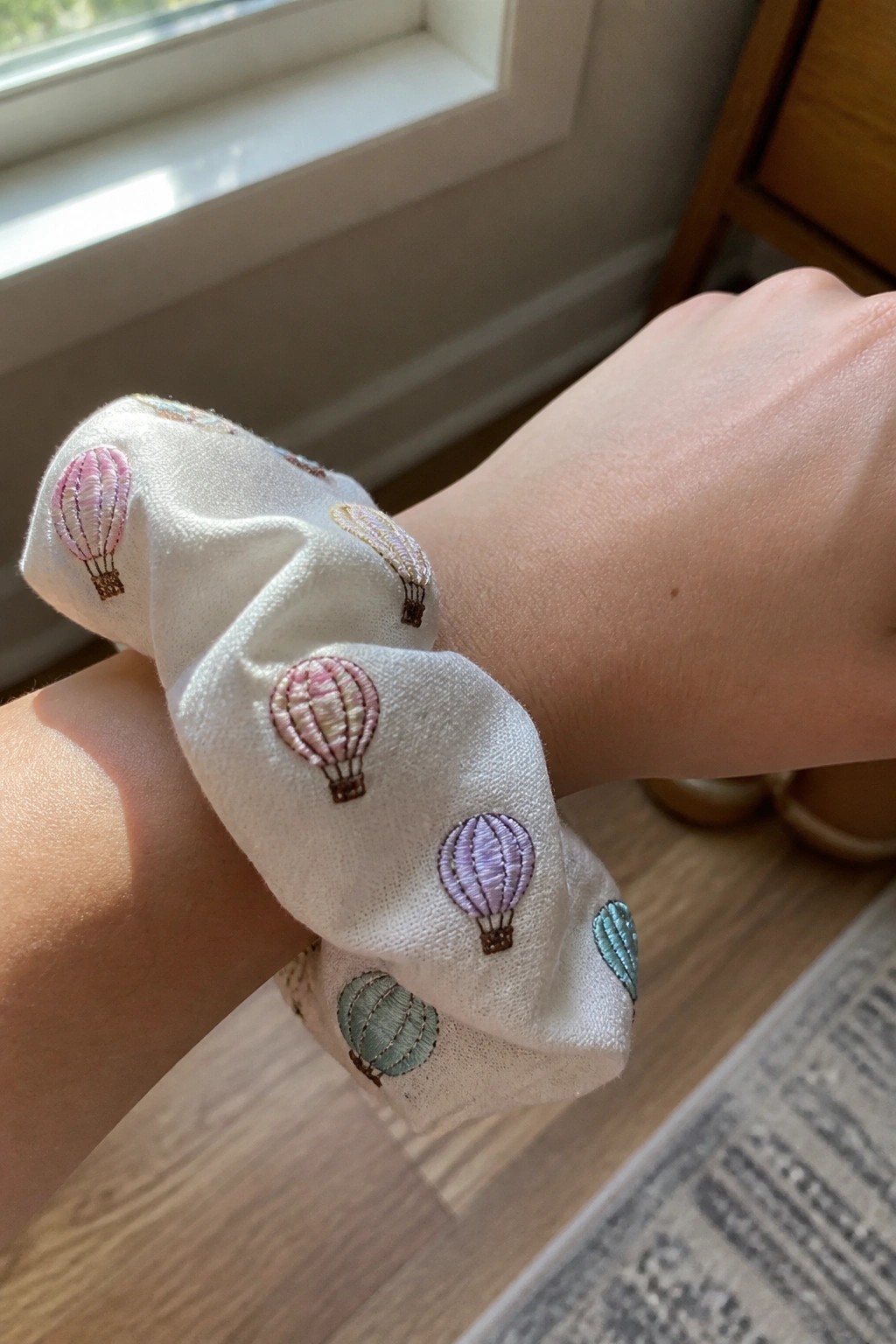 White scrunchie with pastel embroidered hot air balloons on a wrist