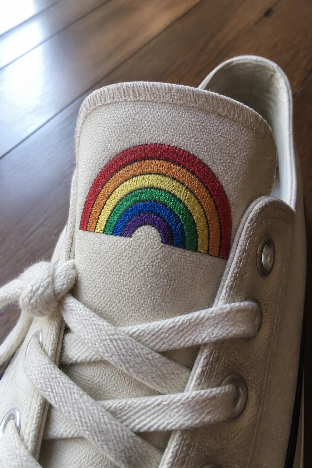 Close-up of a white canvas sneaker showing a rainbow embroidered in curved bands on the heel tab.