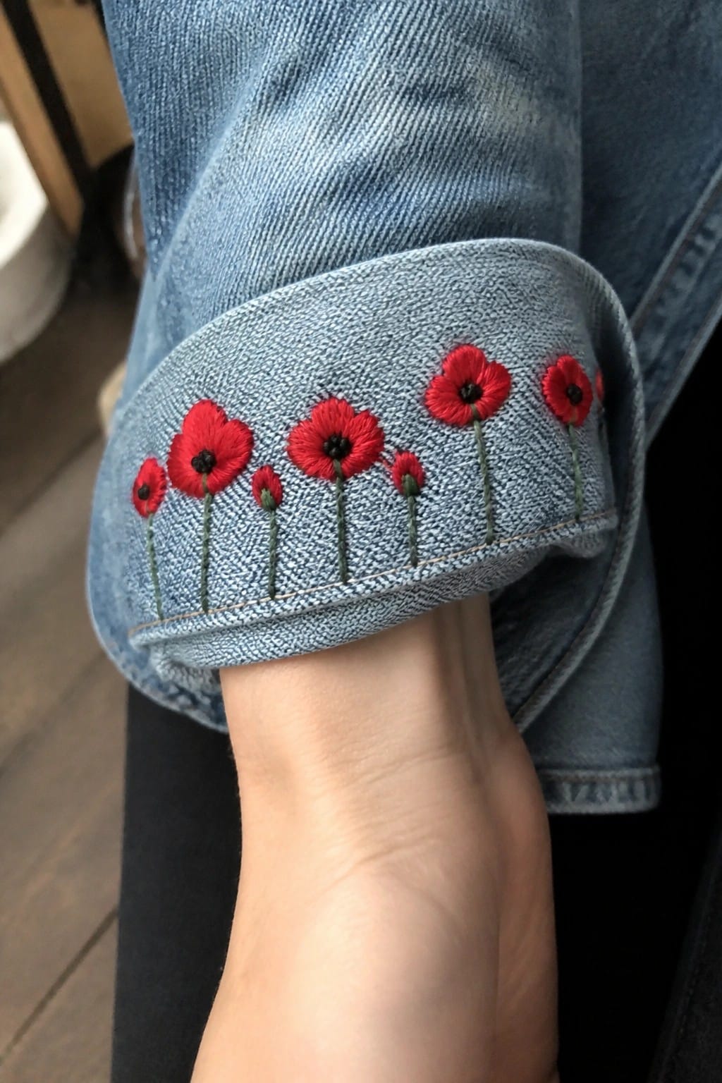 Embroidered red poppies on the cuff of a light blue denim jacket.