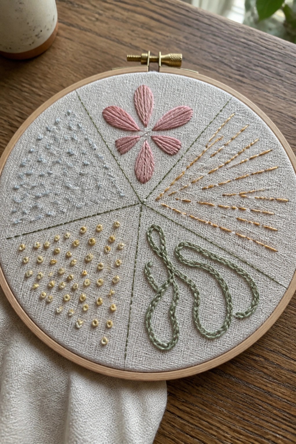 Embroidery hoop with pink flower and colorful stitch patterns in sections.