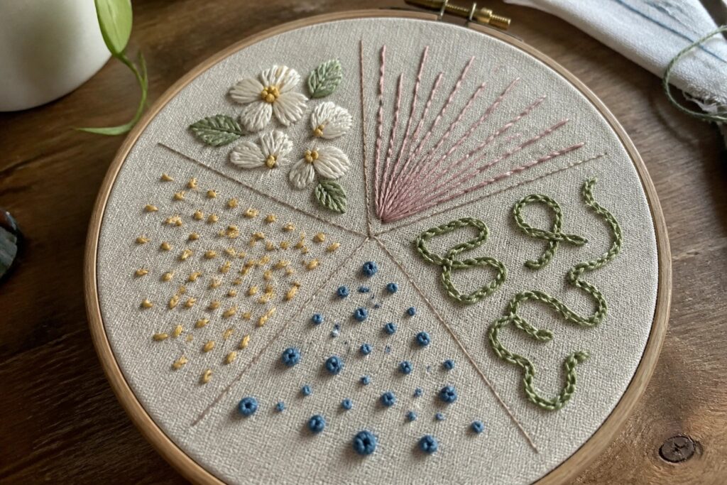 24 Practical Embroidery Sampler Ideas to Practice Stitches and Build Skill Embroidery hoop with pink flower and colorful stitch patterns in sections.
