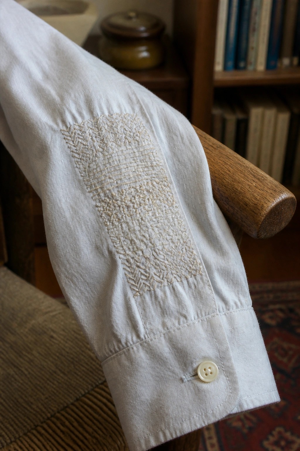 White shirt sleeve with intricate elbow embroidery, buttoned cuff on wooden chair arm.