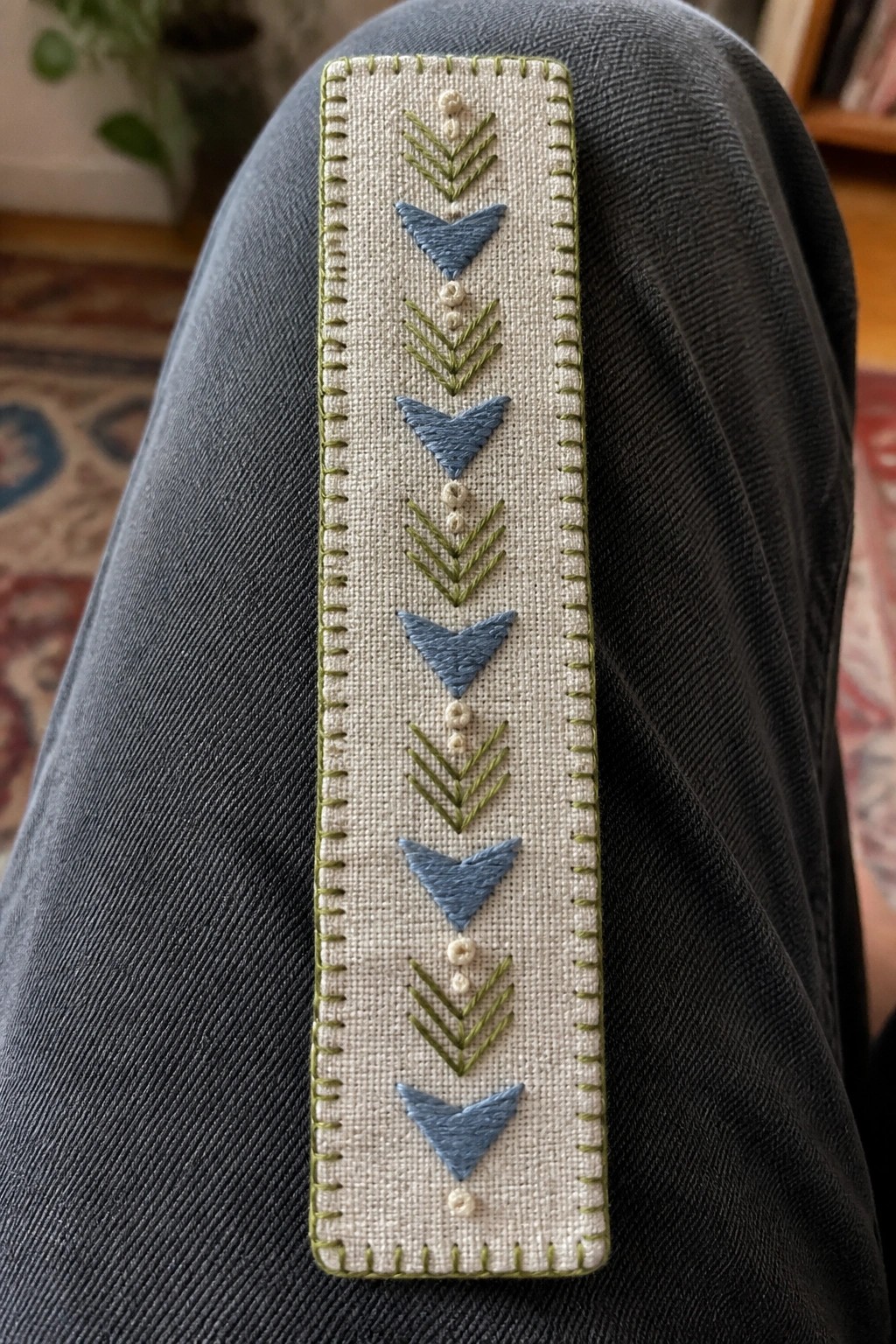 Blue denim pants leg with vertical embroidered panel of blue triangles and green chevrons.