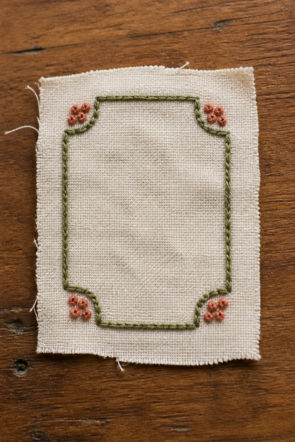 White fabric with green embroidered border and orange corner clusters on wood