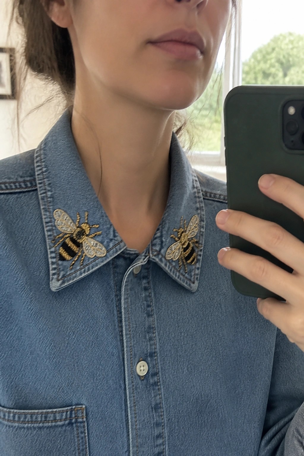 Blue denim shirt with embroidered bees on collar, hand holding green phone