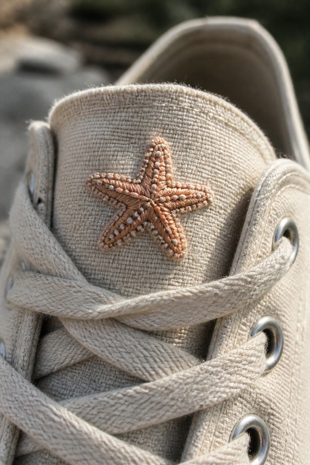 Beige canvas sneaker tongue with embroidered starfish above crossed laces.
