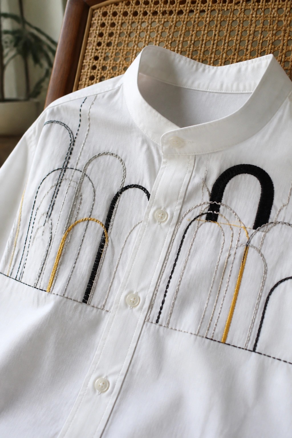 White shirt with colorful arched embroidery on wooden rattan chair.
