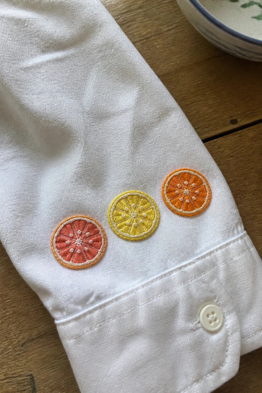 White shirt cuff with embroidered pink, yellow, and orange citrus slices and button.