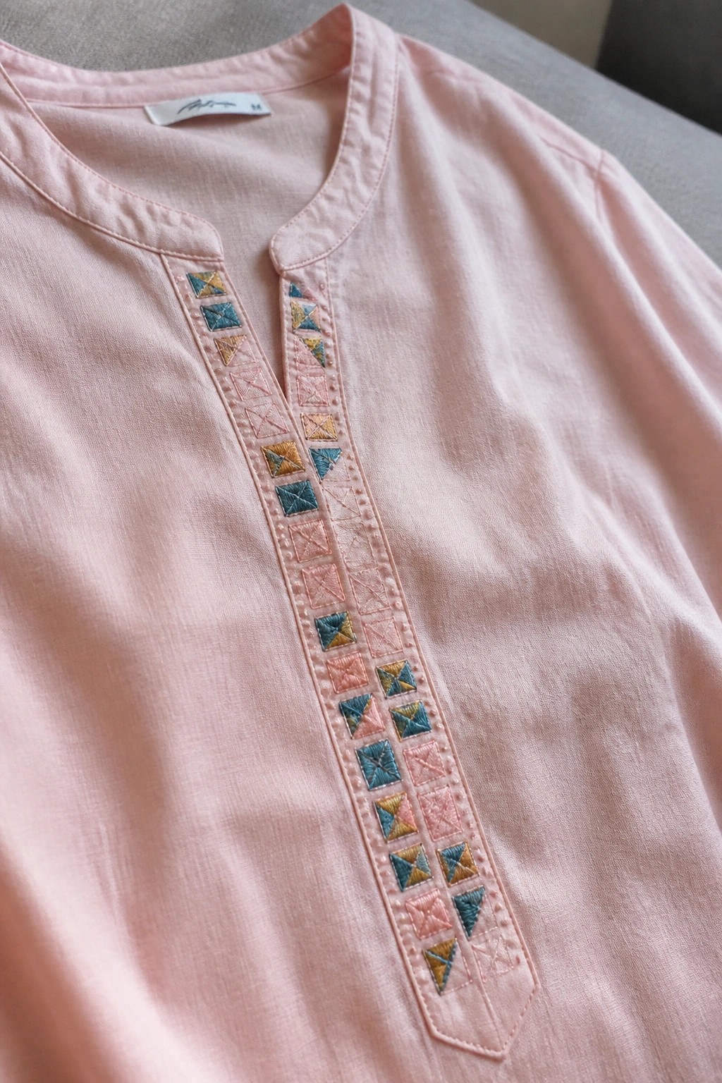 Pink shirt with colorful geometric embroidery along the placket and neckline.