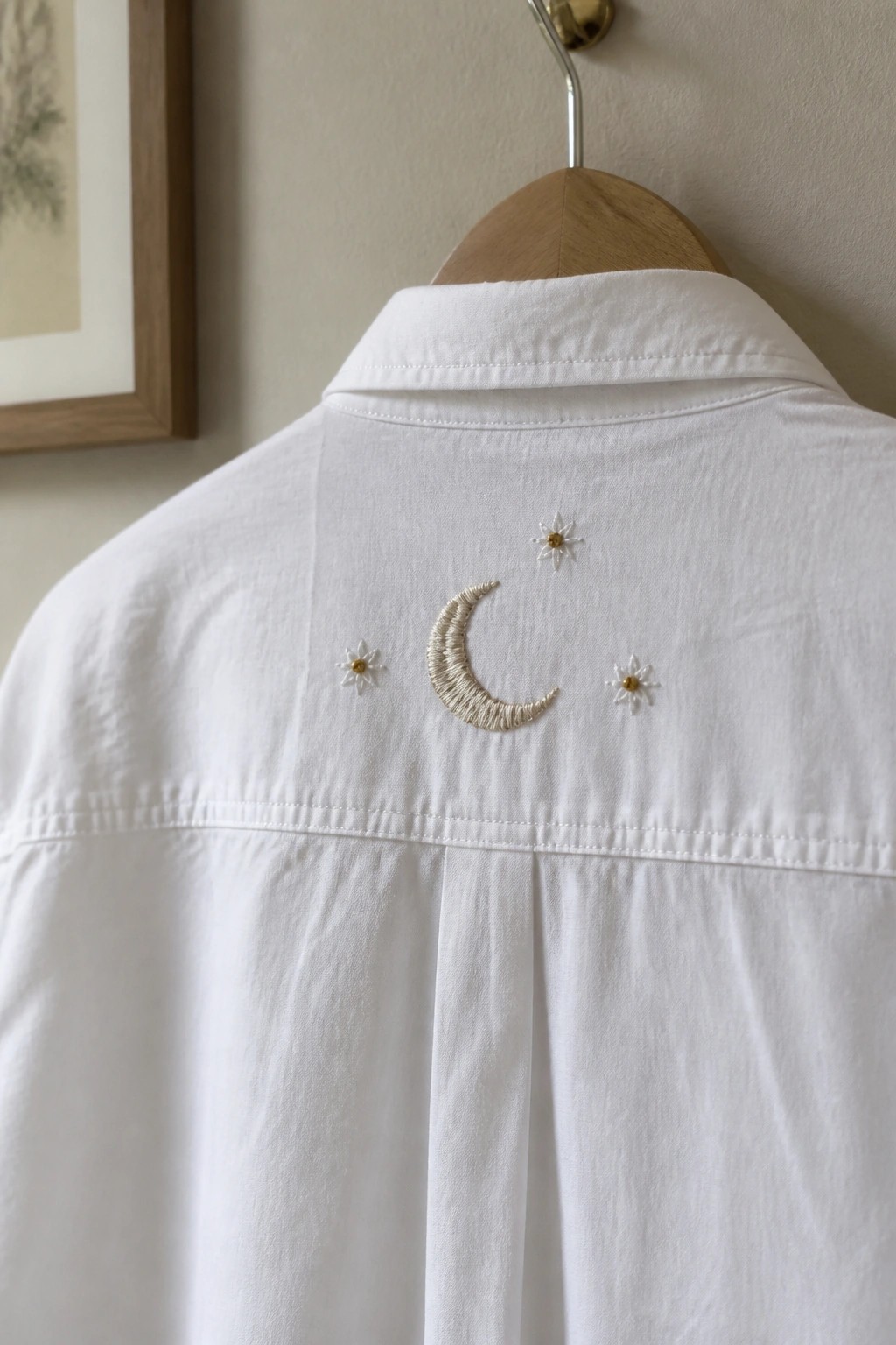 White collared shirt with embroidered crescent moon and stars on wooden hanger.