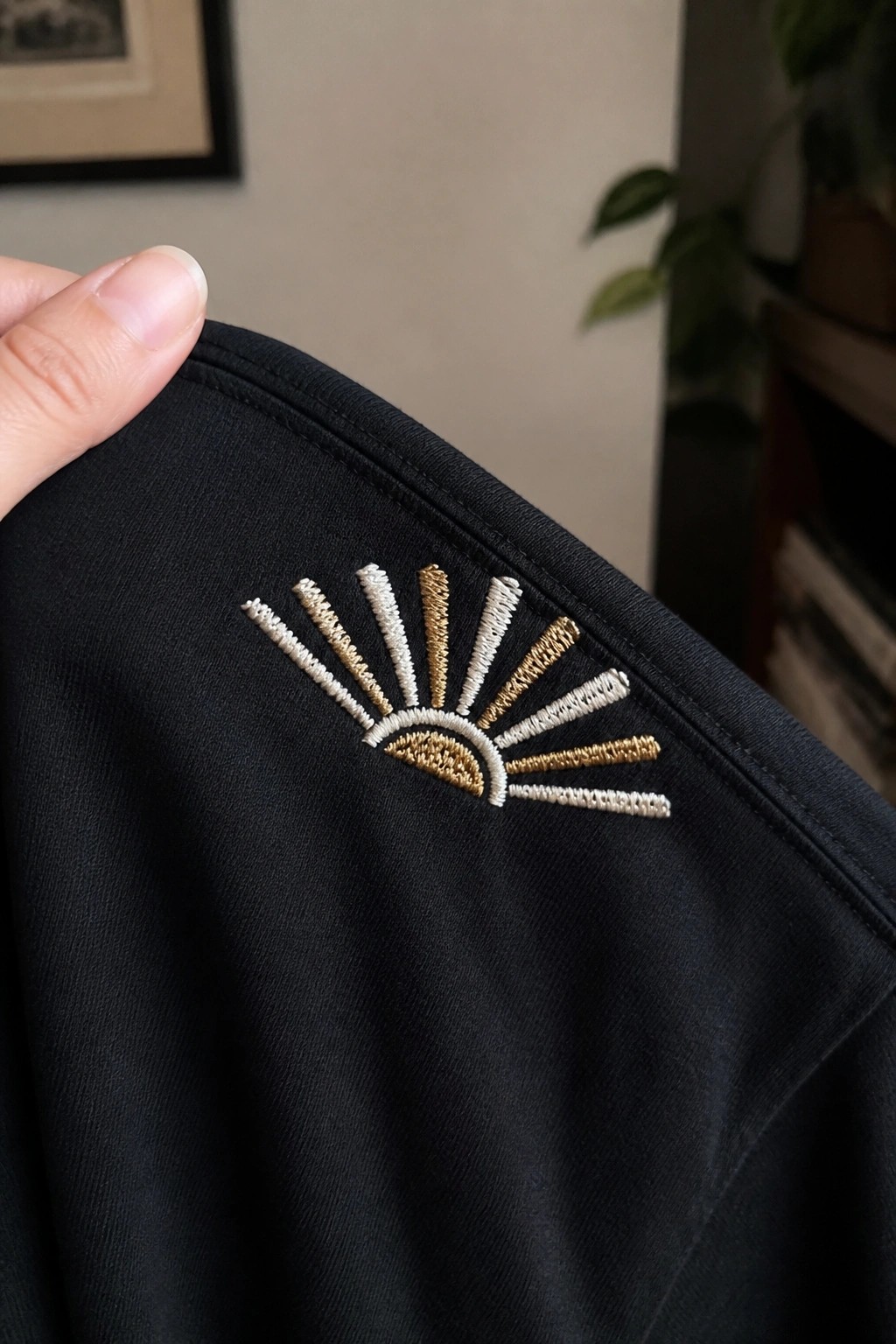 Black garment with white and gold embroidered sunburst design, held by hand