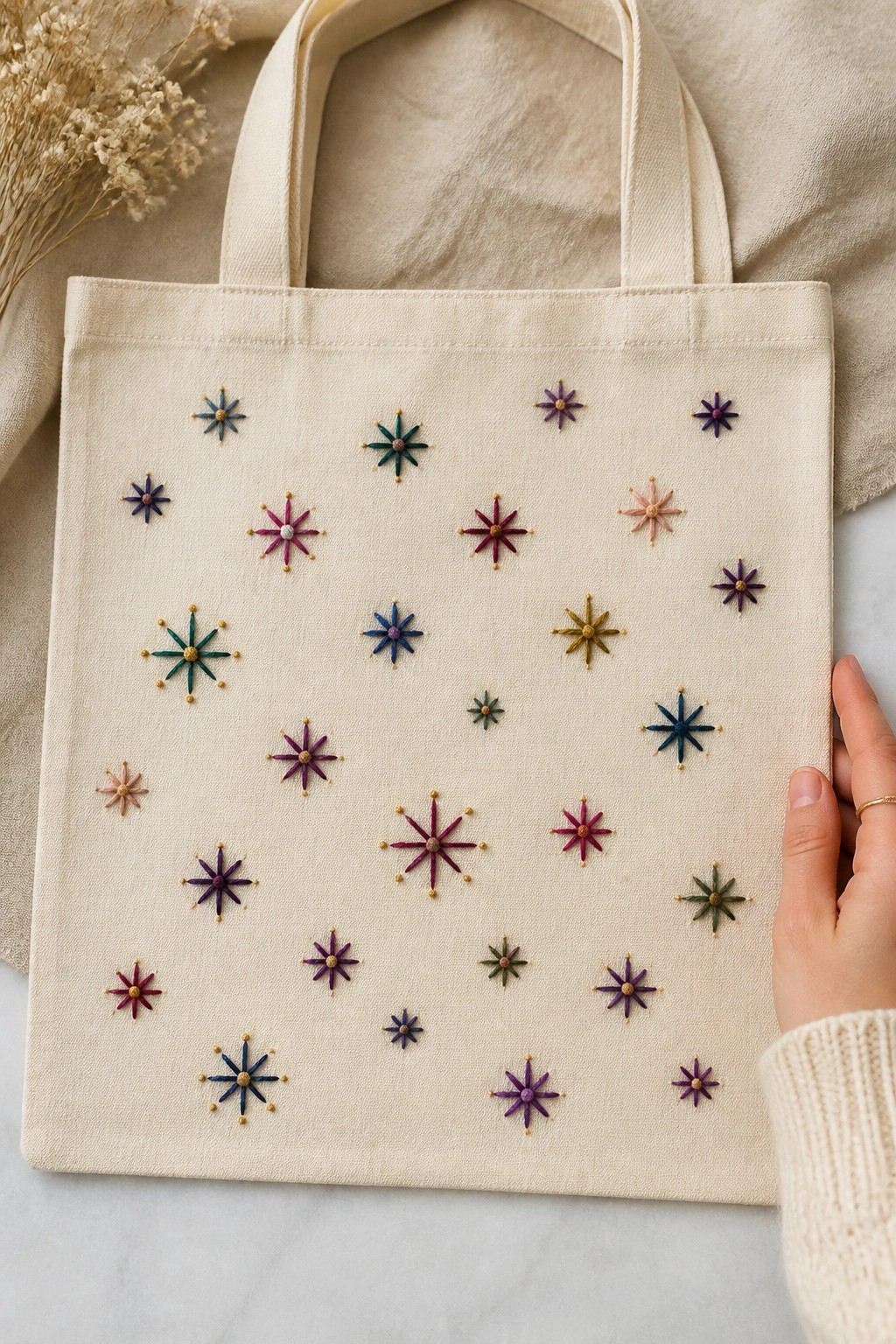 Beige tote bag with colorful embroidered stars held by a hand on fabric