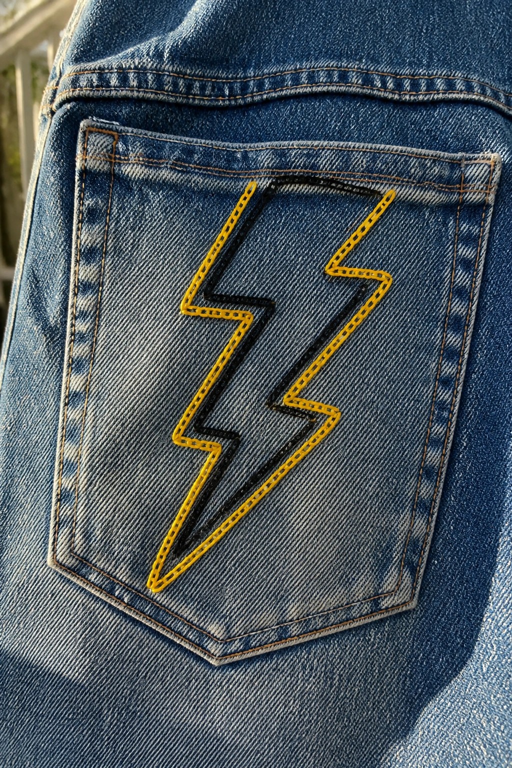 Blue denim jeans pocket with yellow lightning bolt embroidery outlined in black.