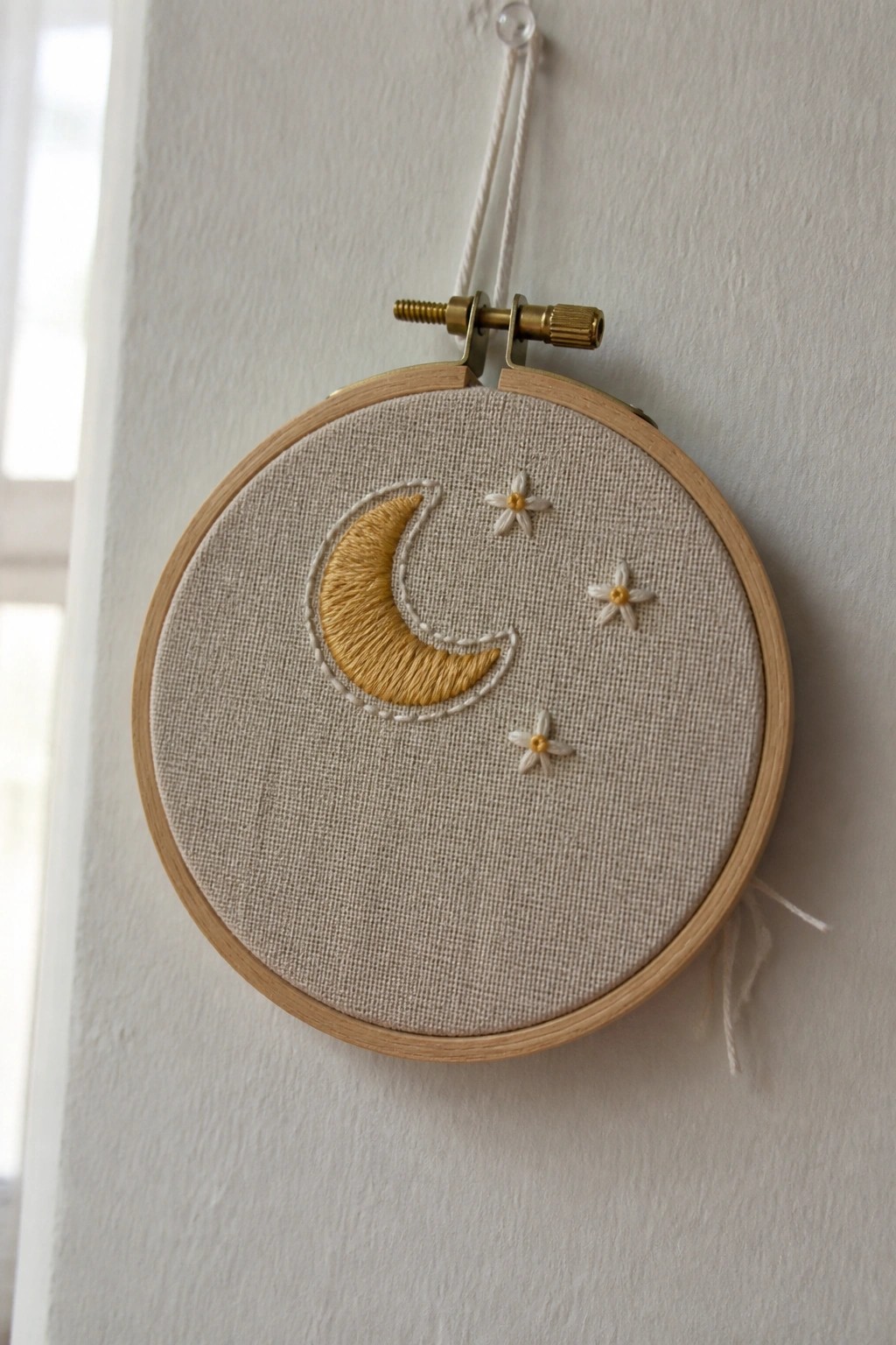 Wooden hoop holding beige fabric embroidered with golden moon and white star flowers.