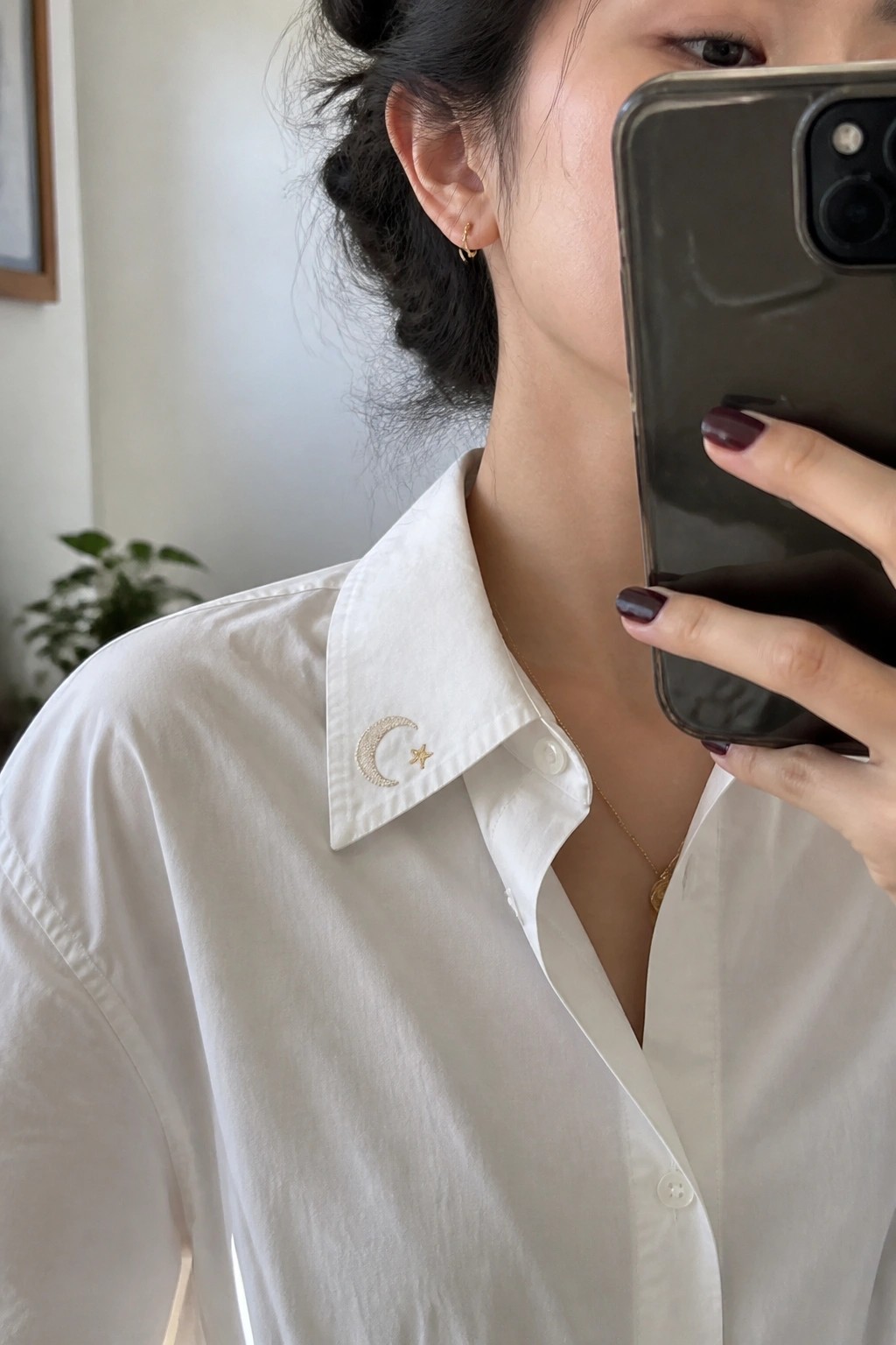 Woman in white collared shirt with moon-star embroidery holding smartphone