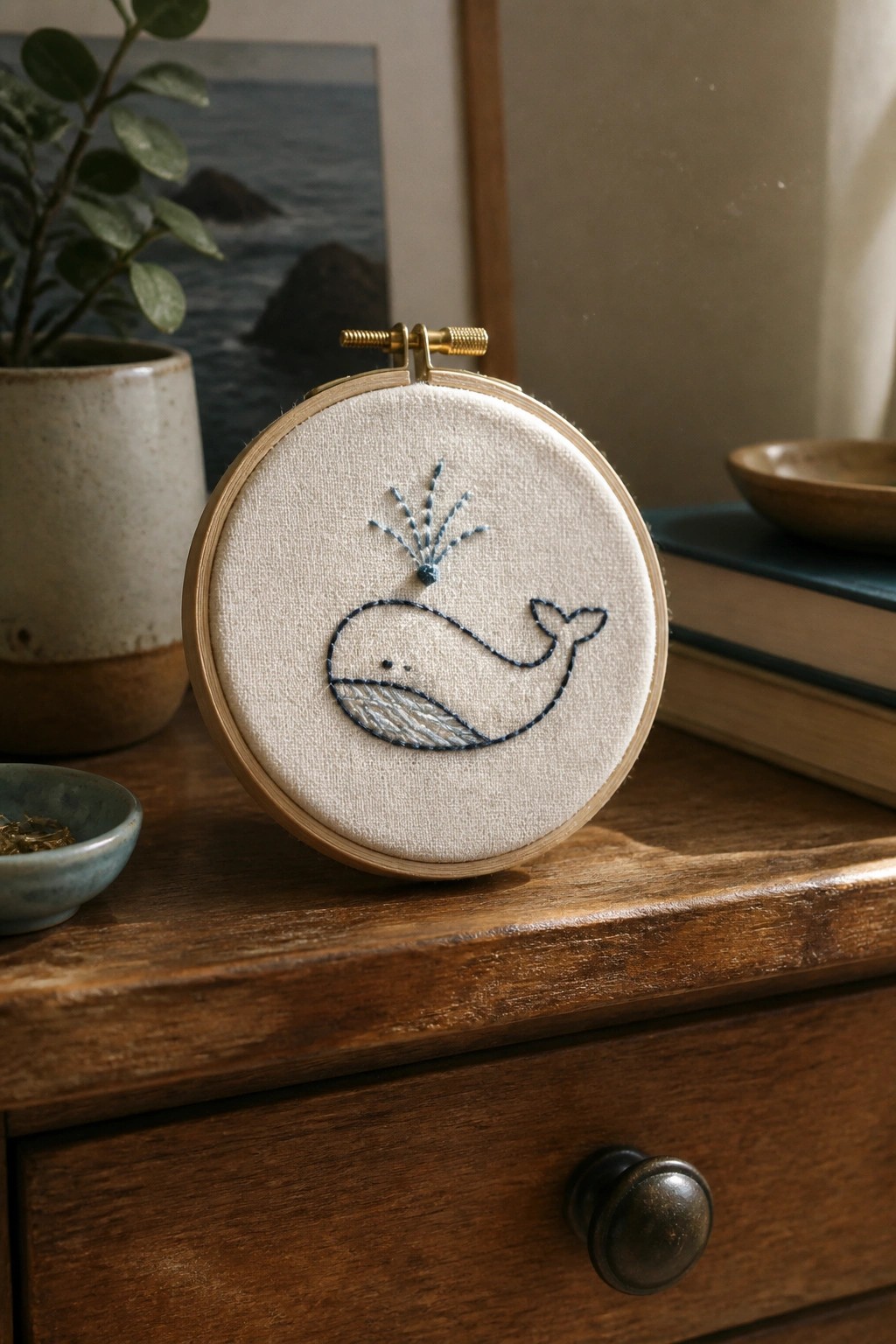 Wooden embroidery hoop with blue whale stitching on a rustic dresser.