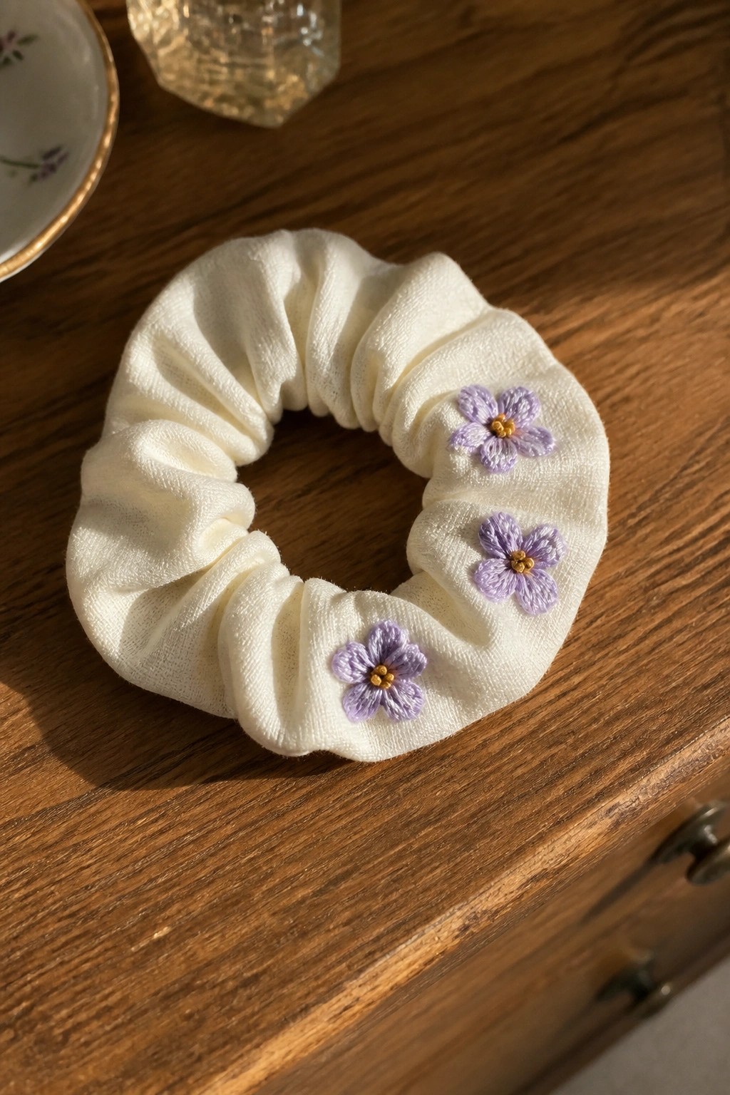 White scrunchie with three purple embroidered flowers on wooden table