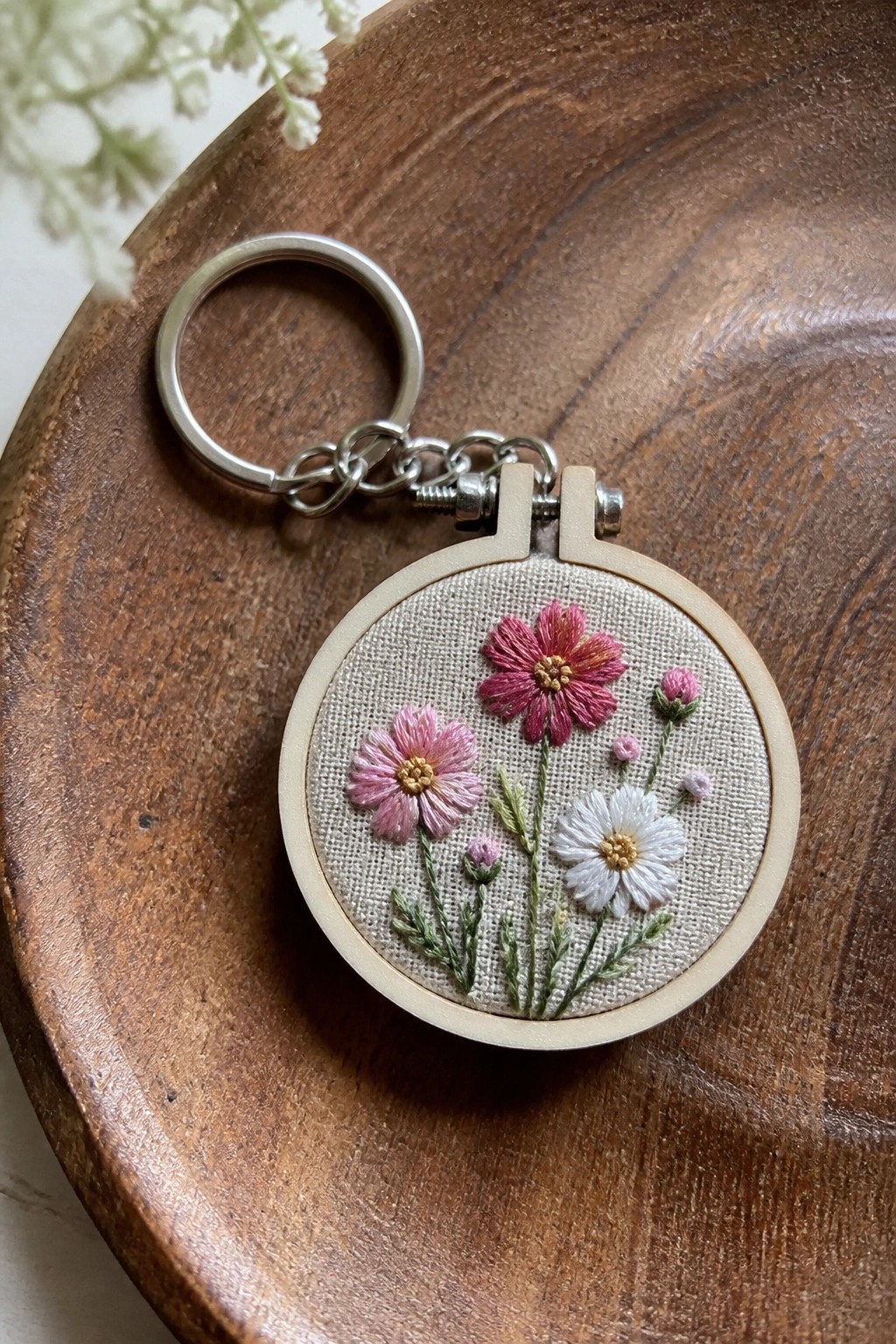 Small embroidery hoop keychain with pink, magenta, and white flowers on beige fabric.