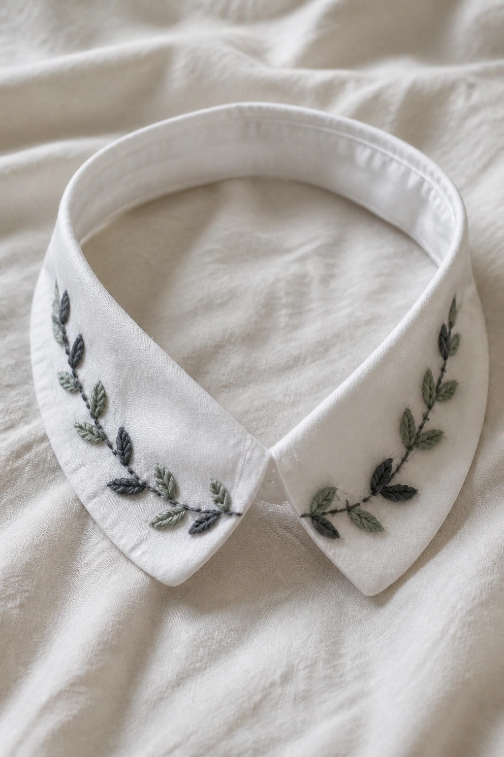 White collared shirt with symmetrical green and gray embroidered leaf vines.