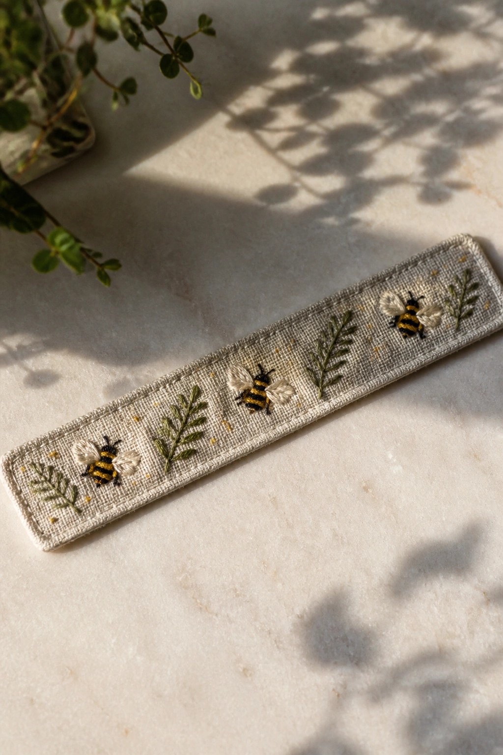 Narrow beige fabric strip embroidered with three bees, green leafy branches, and scattered yellow dots.