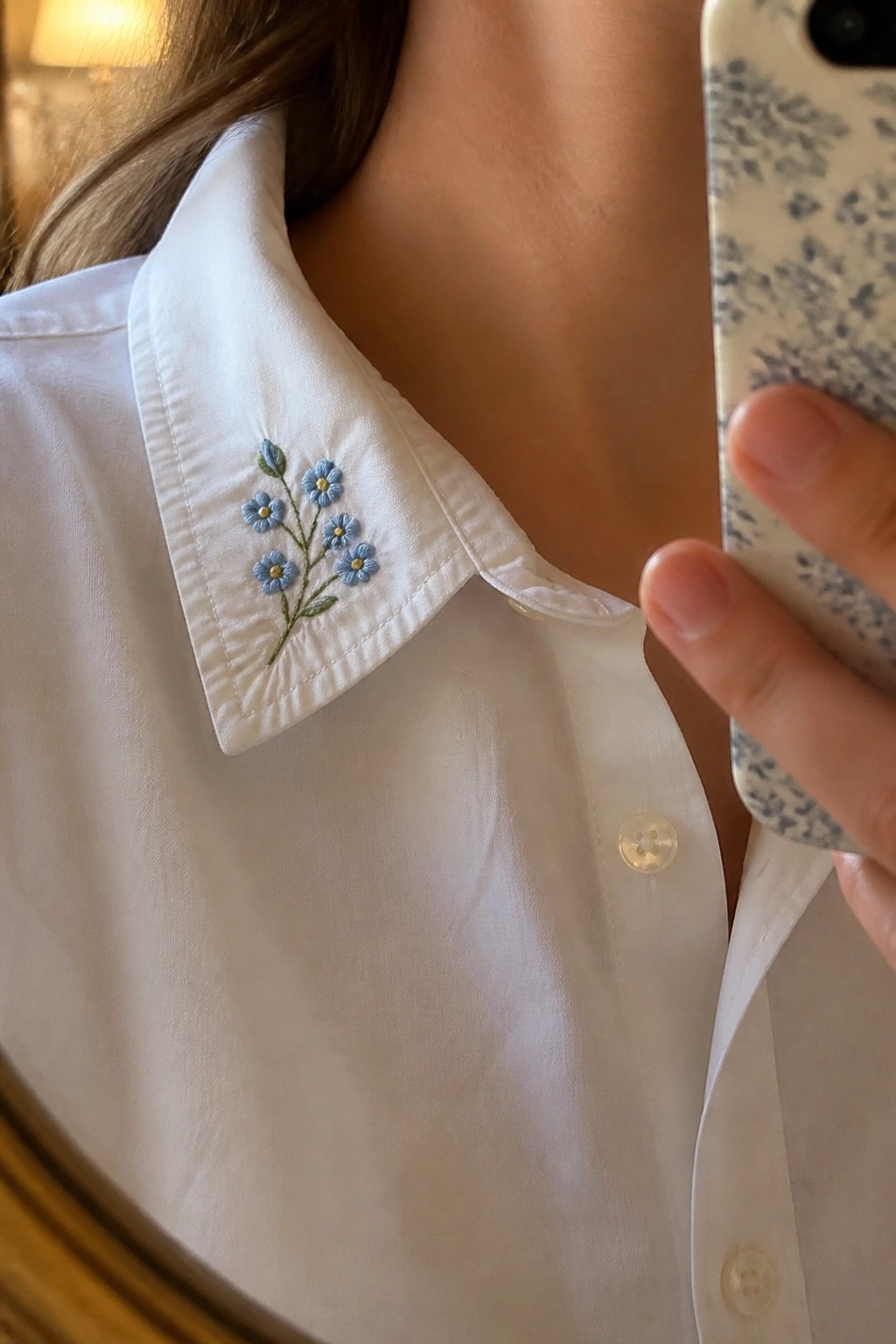White shirt collar with blue floral embroidery, hand holding patterned phone