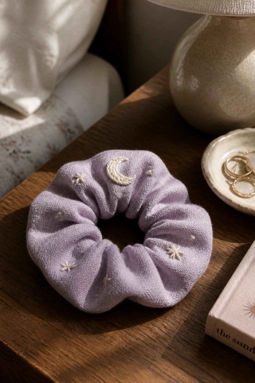Lavender scrunchie with white crescent moon and star embroidery on wooden table