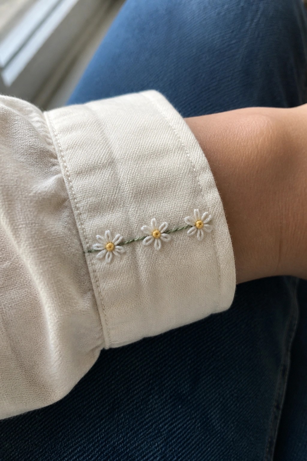 White shirt cuff with three embroidered daisies and green stem line