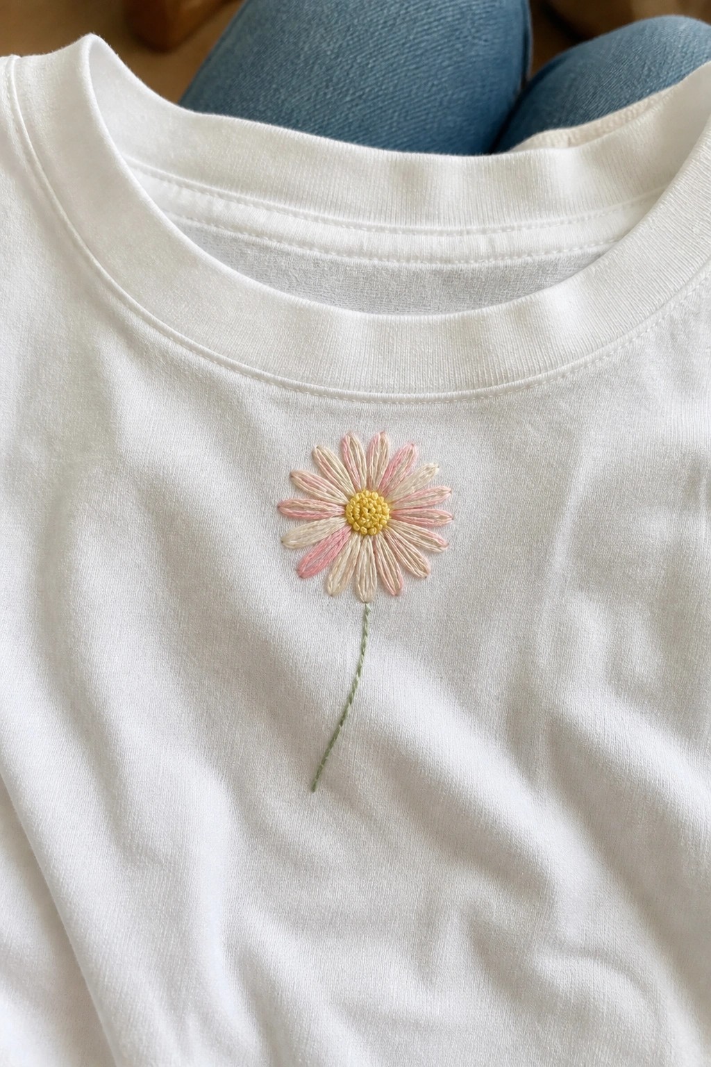 Close-up of a white t-shirt with a small embroidered daisy near the neckline.