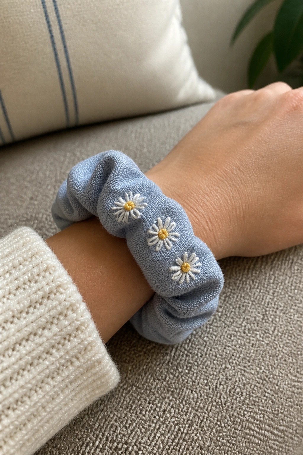 Light blue scrunchie with daisy embroidery on wrist with white sweater sleeve.