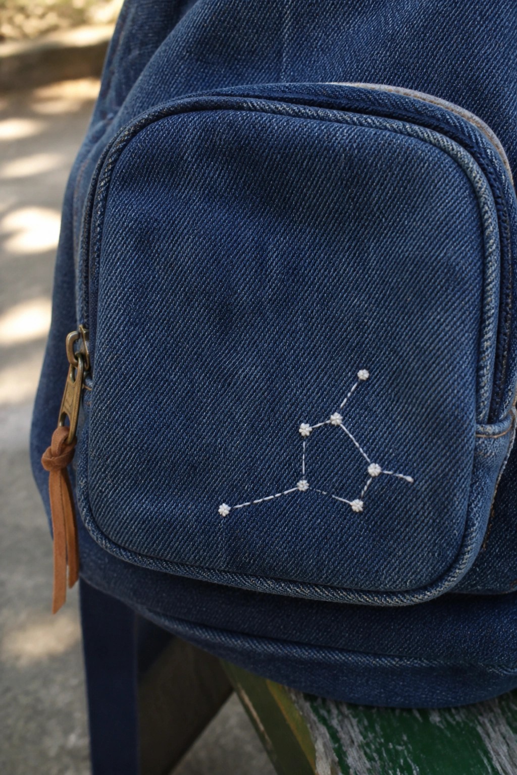 Close-up of white constellation embroidery on the front pocket of a blue denim bag.