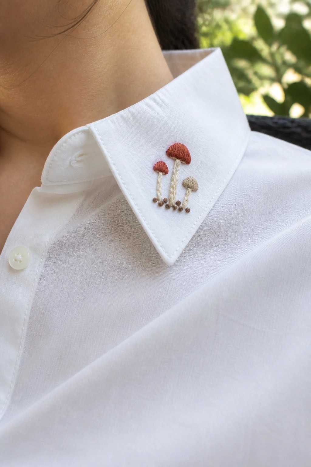 Three small embroidered mushrooms on the collar of a white button-up shirt.