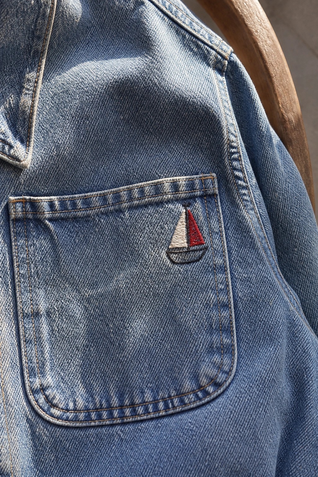 Blue denim jacket pocket with embroidered sailboat in white and red sails.