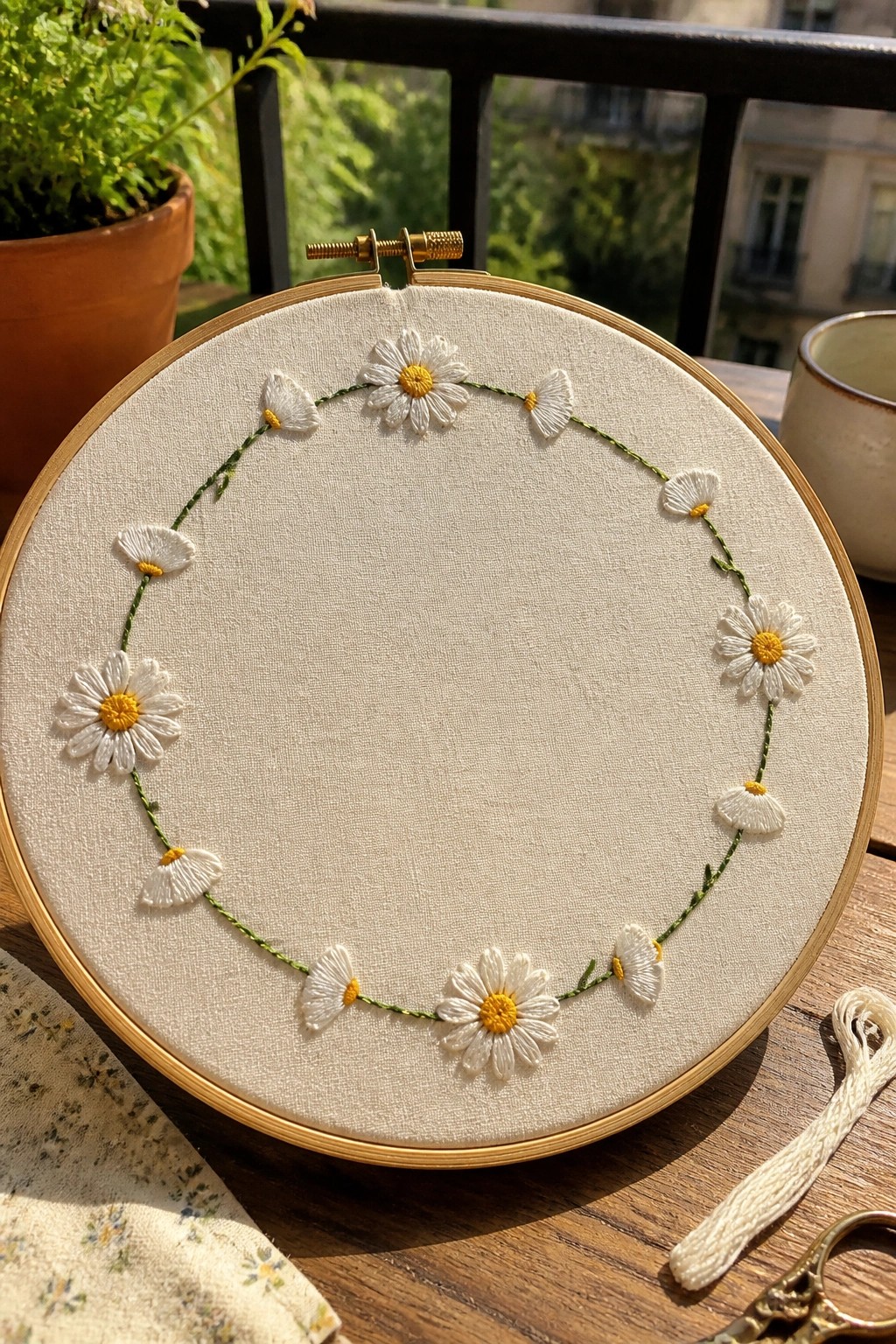 Embroidery hoop with circular wreath of white daisies and yellow centers on fabric.
