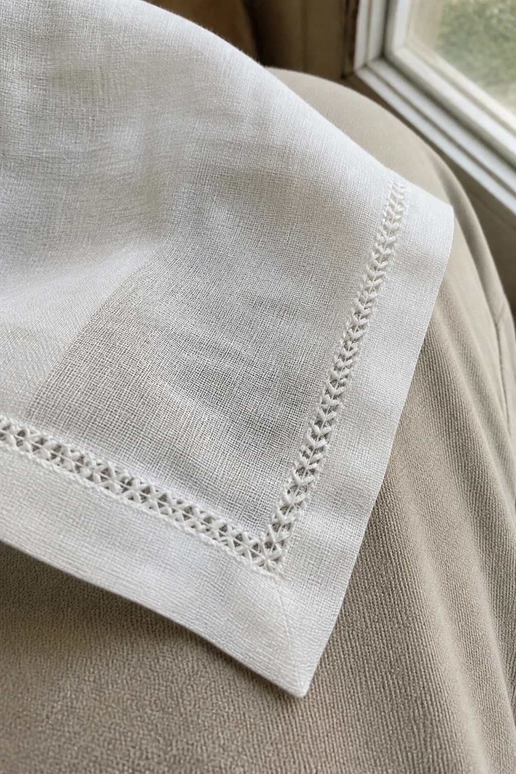White linen fabric with intricate white embroidery border on beige surface near window.
