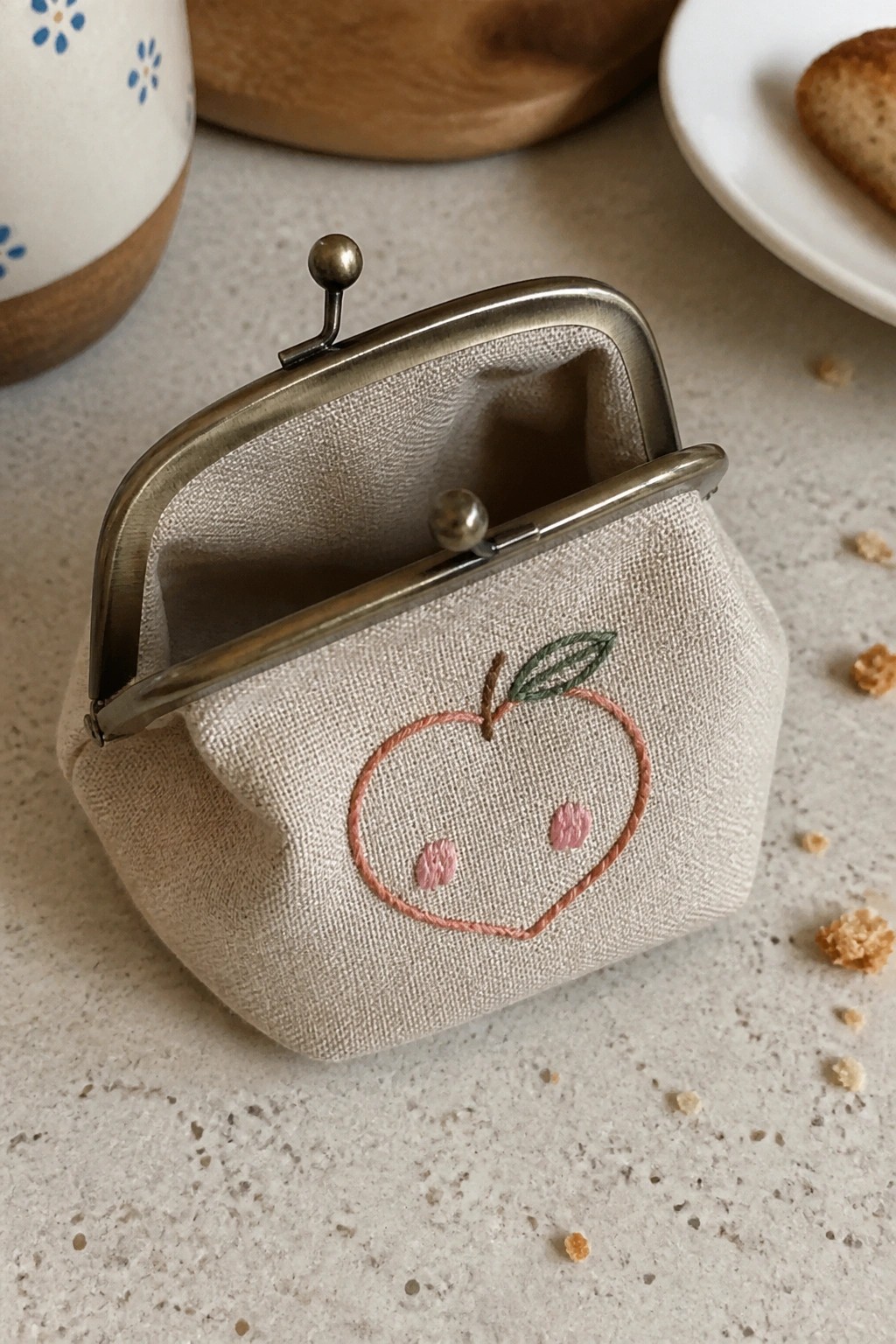 Open beige coin purse with embroidered peach face and metal clasp on countertop
