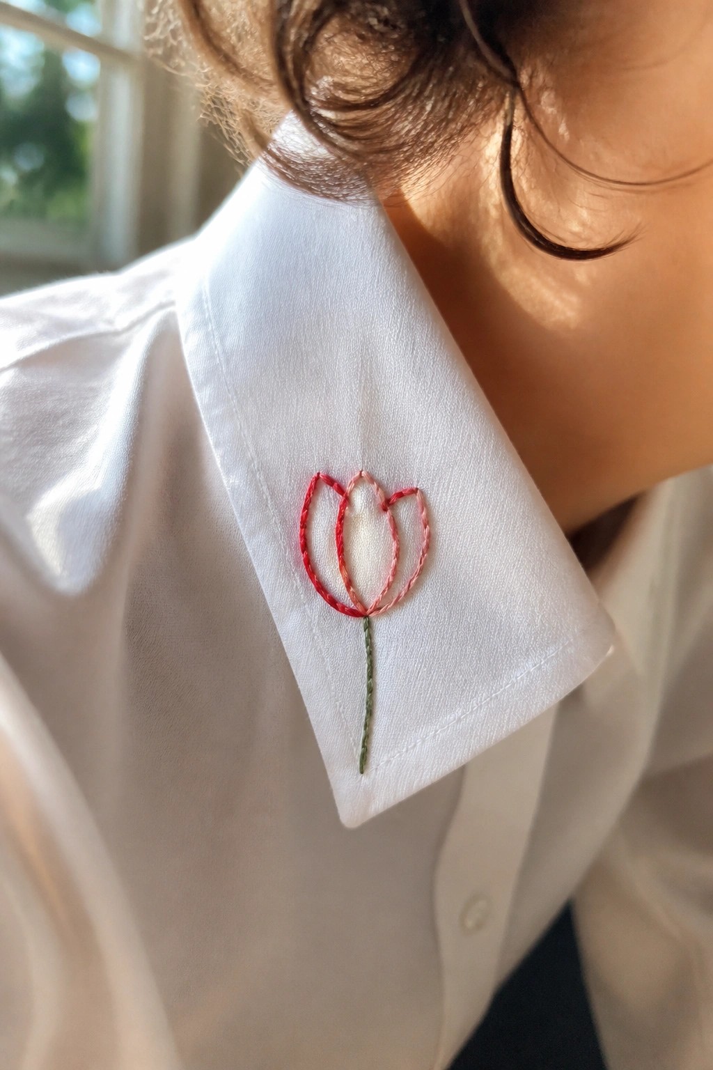 White shirt collar with embroidered red-pink tulip and green stem.