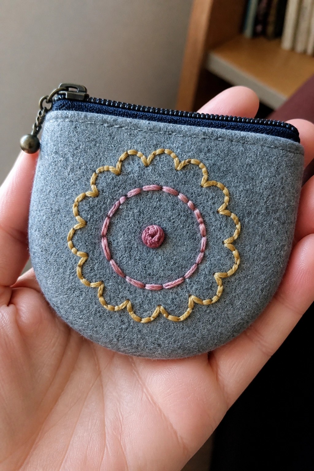 Hand holding gray felt coin purse with blue zipper and yellow-pink flower embroidery