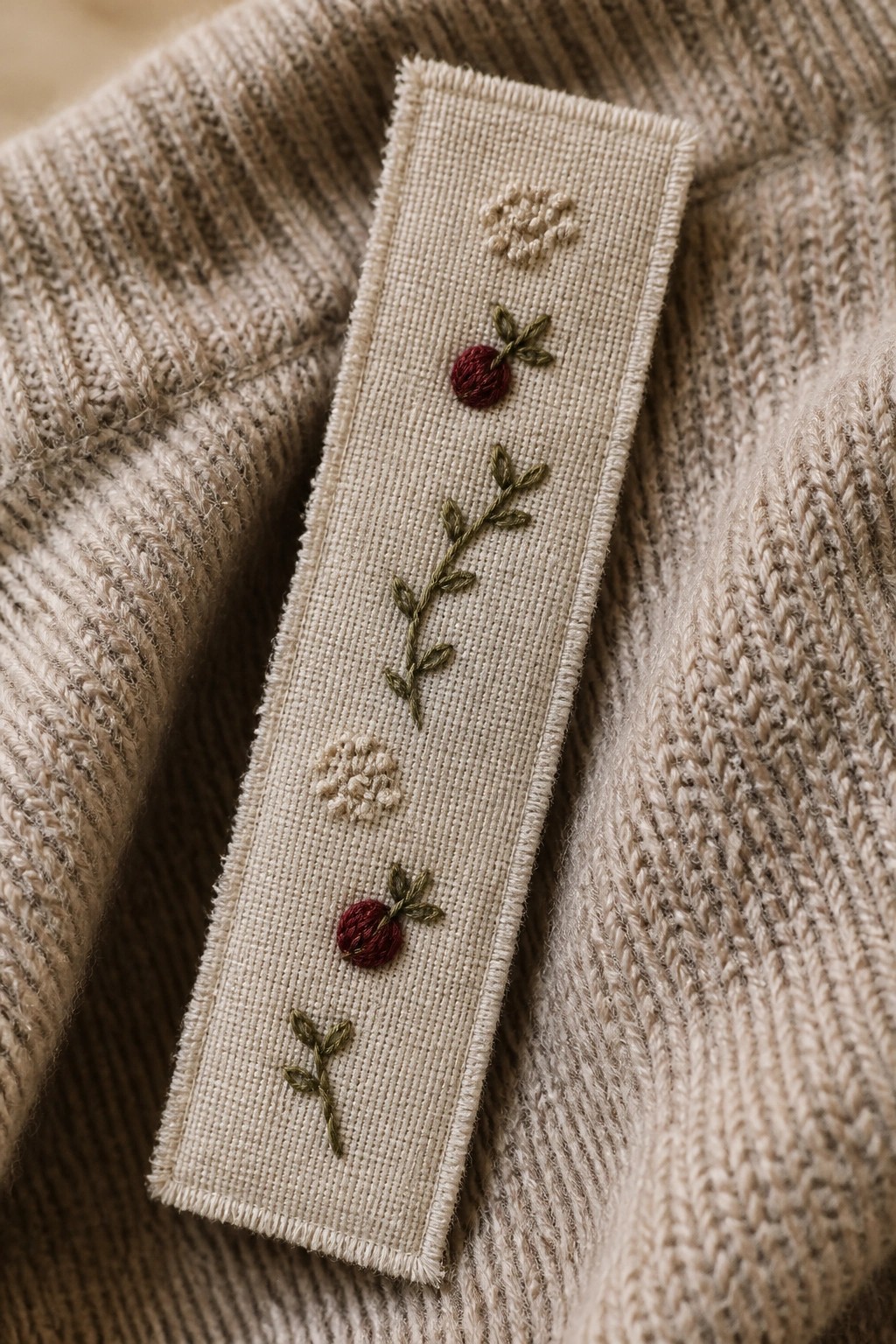 Embroidered bookmark with red berries and green leaves on beige knit sweater