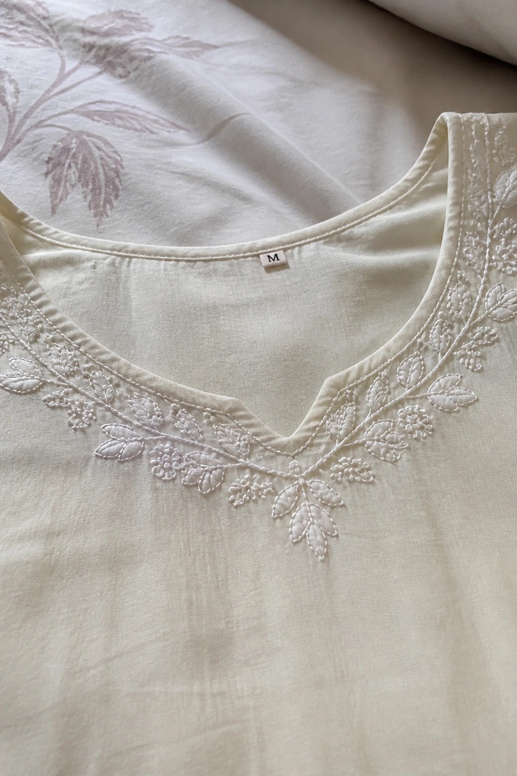 Cream blouse neckline with white floral embroidery and visible M size tag.