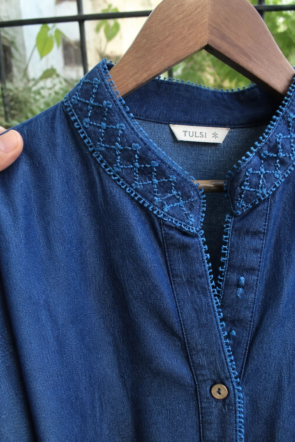 Blue denim blouse with intricate blue embroidery on collar, on wooden hanger