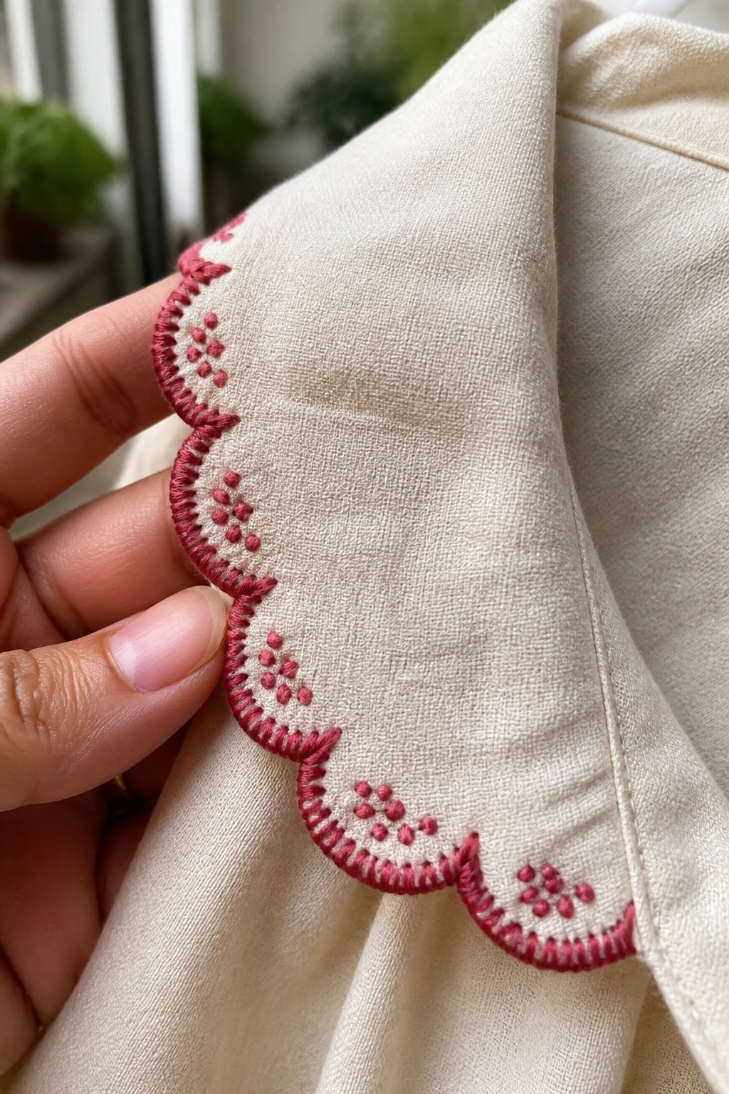 Hand holding cream fabric with pink scalloped embroidery along the edge