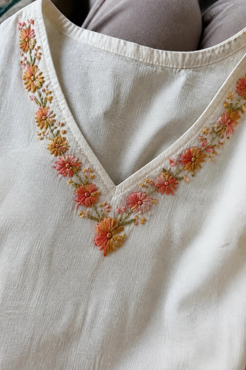 White V-neck top with colorful floral embroidery in pink, orange, and yellow
