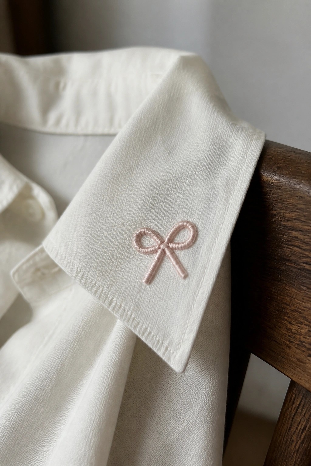 White shirt collar with delicate pink bow embroidery on wood