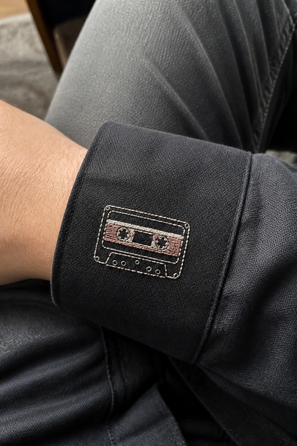 Black denim jacket cuff with embroidered cassette tape patch near wrist.