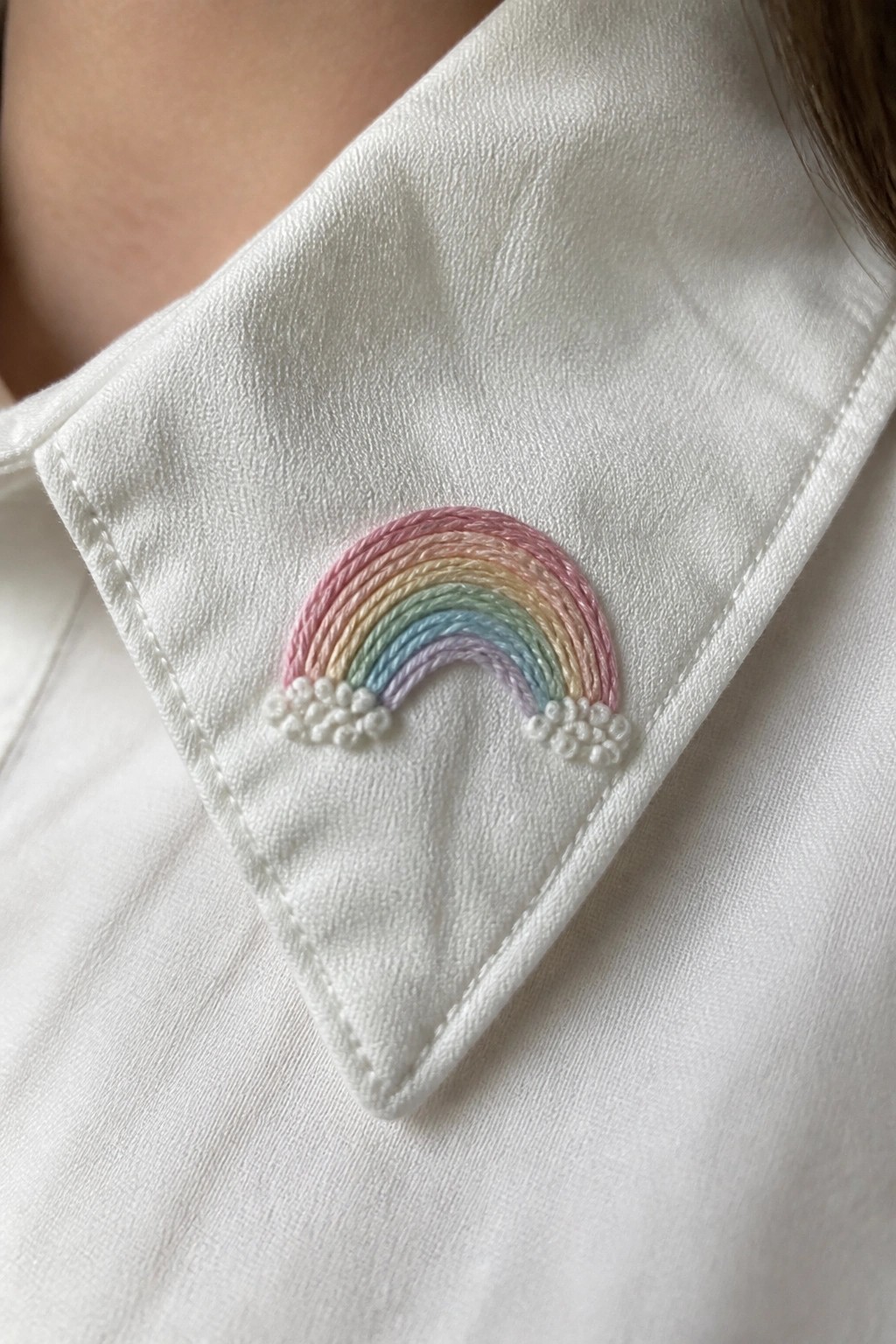 Close-up of white shirt collar with small pastel rainbow embroidery and white clouds at each end.
