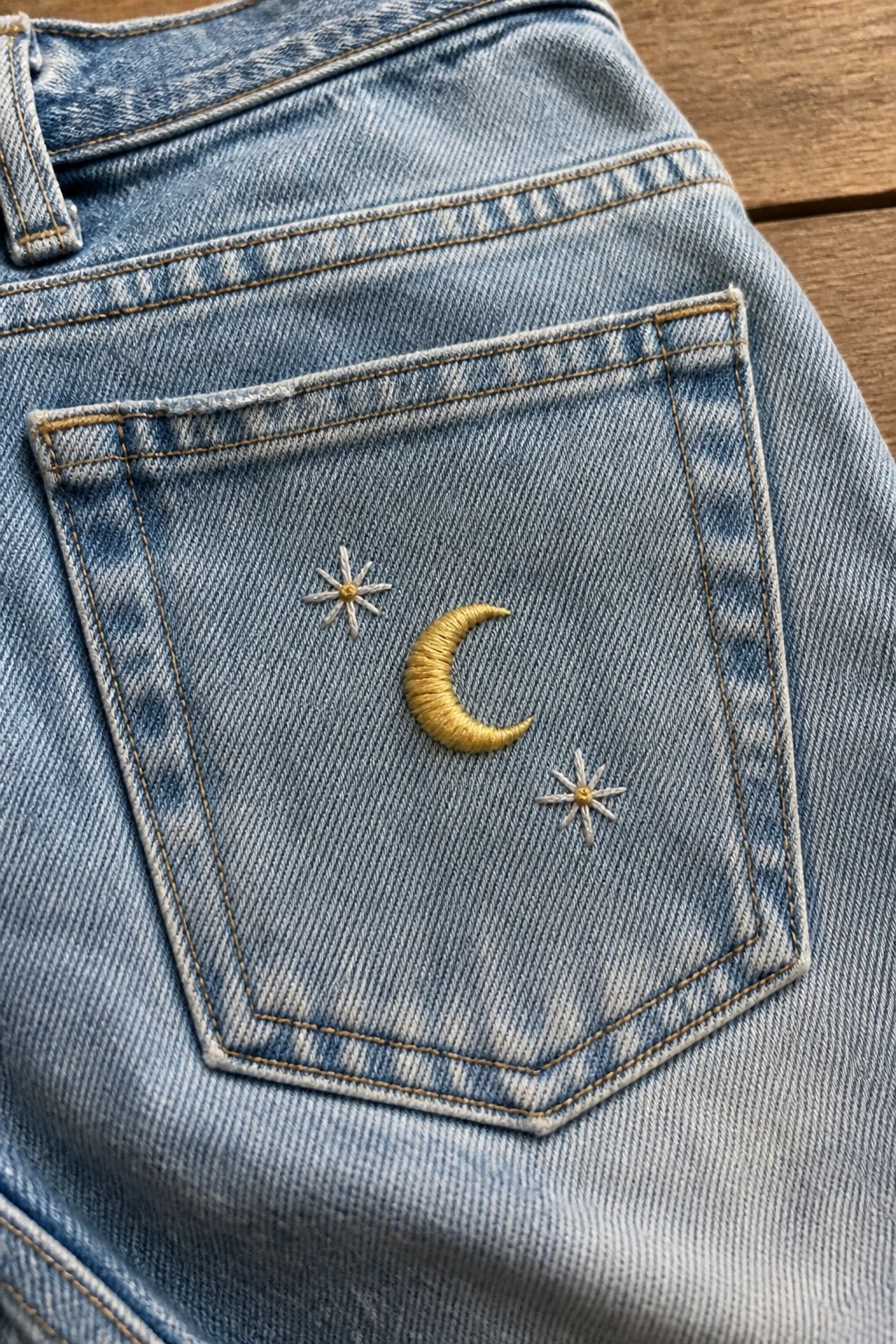 Light blue denim jeans back pocket with gold crescent moon and star embroidery.