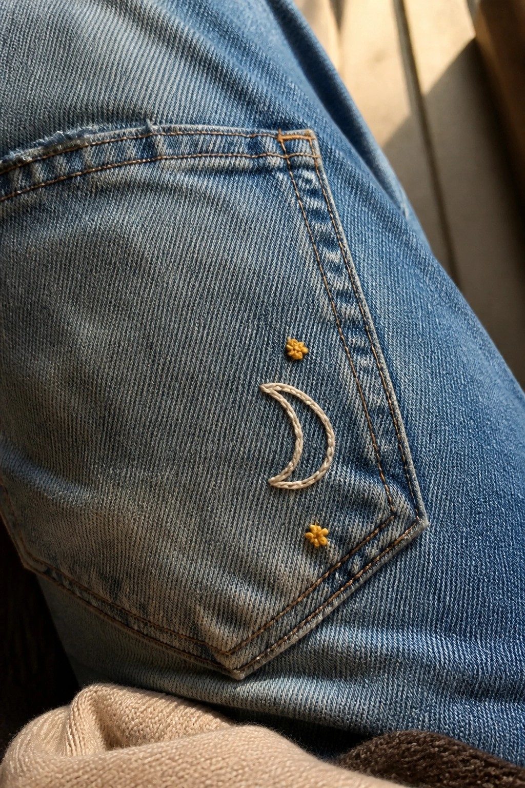 Blue denim jeans pocket with embroidered white crescent moon and yellow flowers